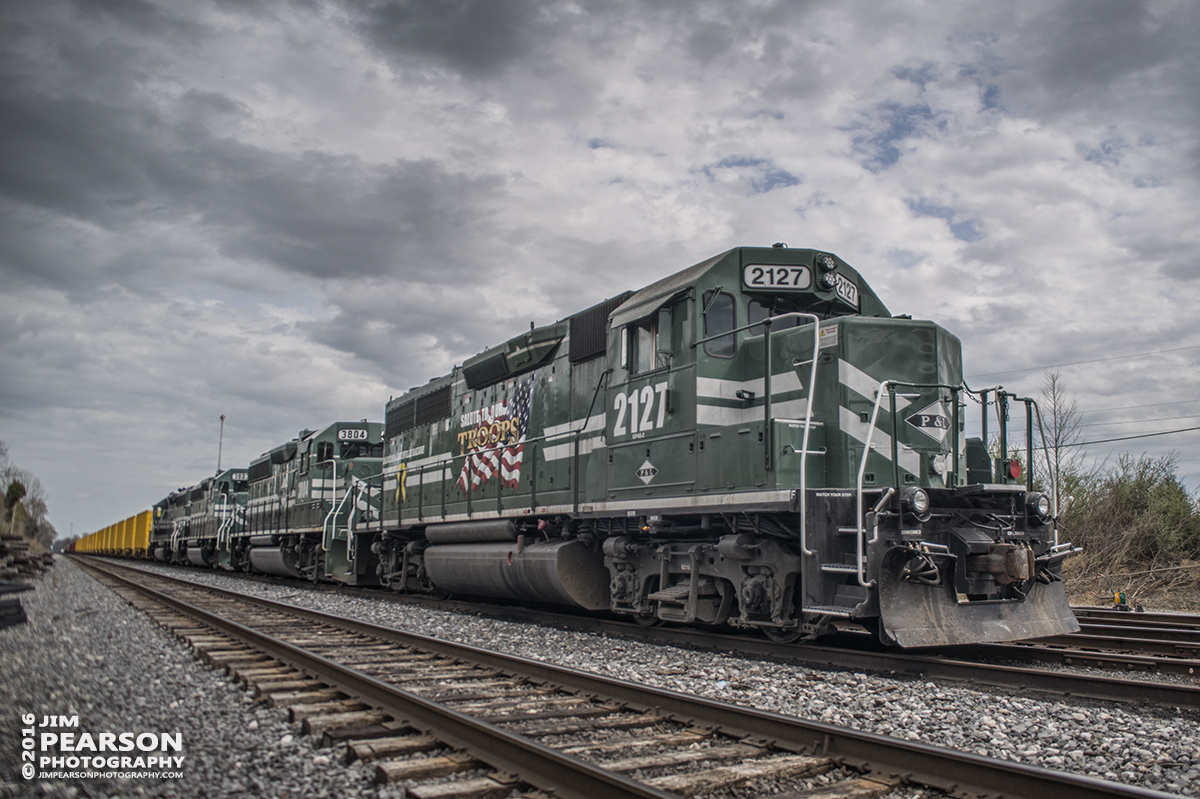 March 30, 2016 - Paducah and Louisville Railway "Support our Troops" engine 2127 heads up a ballast train sitting in the number 2 track at West Yard in Madisonville, Ky waiting for a crew to take it on south to pickup a load of rock. - Tech Info: 1/250 | f/2.8 | ISO 100 | Lens: Sigma 24-70 @ 24mm on a Nikon D800 shot and processed in RAW.