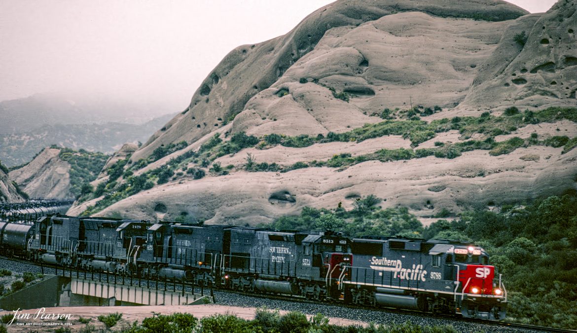 A Southern Pacific tank train makes it's way through the Cajon Pass in Sothern California in March of 1995 with 5 units pulling hard.

I spent a lot of years railfanning the pass between 1981 and 1995! It's a great place to catch trains and I've been back several times over the years since then.

In fact I'm headed back again this coming September for a week or so to see how much it has changed since I was last there several years ago. In fact, it was before I had a drone, so I'm really looking forward to railfanning from the air this next trip!

According to Wikipedia: Cajon Pass is a mountain pass between the San Bernardino Mountains to the east and the San Gabriel Mountains to the west in Southern California. Created by the movements of the San Andreas Fault, it has an elevation of 3,777 ft (1,151 m).[1] Located in the Mojave Desert, the pass is an important link from the Greater San Bernardino Area to the Victor Valley, and northeast to Las Vegas. The Cajon Pass area is on the Pacific Crest Trail.

Cajon Pass is at the head of Horsethief Canyon, traversed by California State Route 138 and railroad tracks owned by BNSF Railway and Union Pacific Railroad. Improvements in 1972 reduced the railroad's maximum elevation from about 3,829 to 3,777 feet (1,167 to 1,151 m) while reducing curvature. Interstate 15 does not traverse Cajon Pass, but rather the nearby Cajon Summit. The entire area, Cajon Pass and Cajon Summit, is often referred to as Cajon Pass, but a distinction is made between Cajon Pass and Cajon Summit.

Nikon F3 Camera, Nikon 70-300mm lens, f/stop and shutter speed not recorded