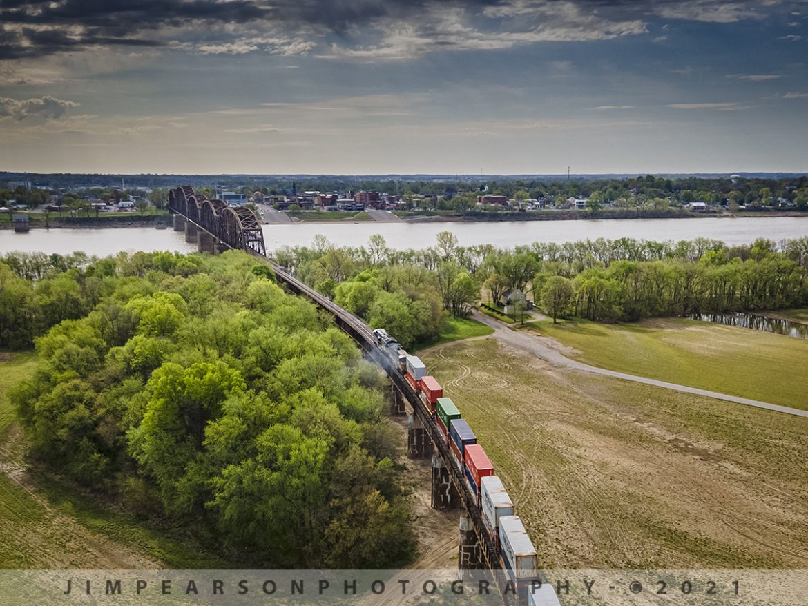 CSX Q025 Southbound prepares to cross the Ohio River

On March 10th, 2021 CSX hot intermodal Q025 pulls up the final stretch of the viaduct as it prepares to cross over the Ohio River bridge at Henderson, Kentucky as it heads south on the Henderson Subdivision from Rahm, Indiana.

According to Wikipedia: The Henderson Bridge is a railroad bridge spanning the Ohio River between Henderson, Kentucky and Vanderburgh County, Indiana and the bridge is owned by CSX Transportation. The original bridge was constructed in 1884 to 1885 by the Louisville and Nashville Railroad at a cost of $2,000,000.

The single-tracked bridge is approximately 3,686 feet long, and its longest span, at 525 feet, was reputed to be the longest trestle span in the world at that time. The bridge runs from the northern edge of Main Street in Henderson to the low water mark on the Indiana side, resting on 15 stone piers. 

It was designed to carry two 118,000-pound engines followed by 60,000-pound coal tenders, and its maximum uniform load capacity was 2,500 pounds per foot. 

A crowd of 8,000 watched the first train cross the bridge on July 13, 1885. Prior to the opening of the bridge, railroad passengers and freight had to be transferred to a ferry for the river crossing.

Tech Info: DJI Mavic Air 2 Drone, RAW, 4.5mm (24mm equivalent lens) f/2.8, 1/640, ISO 100.