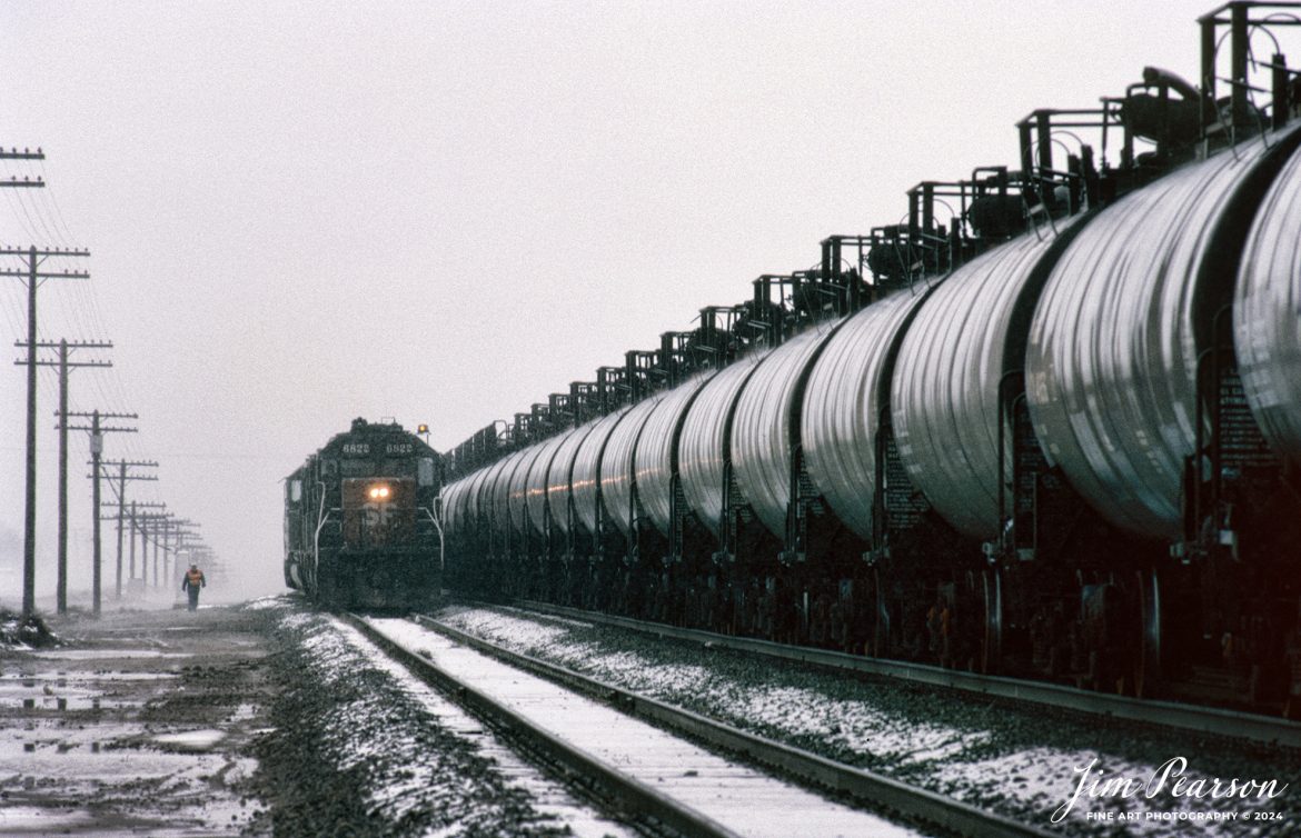 A set of Southern Pacific locomotives sit in the during a late spring snowfall in March of 1995 as the conductor makes his way back to the engines at Devore, California, in the Cajon Pass as they work on a tank train during the cold weather.

According to Wikipedia: Devore Heights, or Devore, is a residential rural neighborhood of the city of San Bernardino, California. It is located just north of the junction of Interstate 15 and Interstate 215, about 12 miles northwest of downtown San Bernardino. It is also the last town to pass through before taking the Cajon Pass to reach Hesperia, California.

Tech Info: Nikon F3 Film Camera, exposure not recorded.

#railroad #railroads #train #trains #bestphoto #railroadengines #picturesoftrains #picturesofrailway #bestphotograph #photographyoftrains #trainphotography #JimPearsonPhotography #trending #southernpaficicrailroad