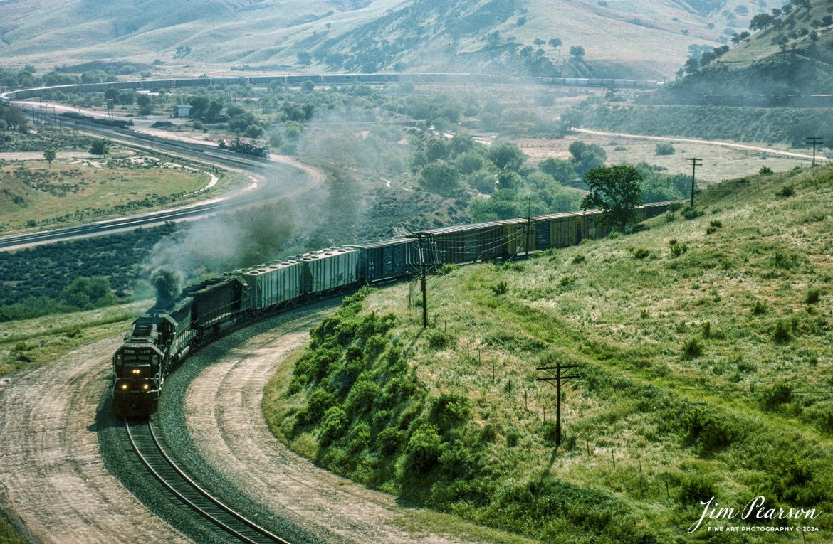 A eastbound heavy freight climbs out of Caliente, which is east of Bakersfield, California in the Tehachapi mountains sometime in the early 1995  in this Kodachrome slide scan.

According to Wikipedia: Established in the 1870s, Caliente was originally named Allens Camp for a cattle rancher and settler named Gabriel Allen. Later, the name Agua Caliente, coming from hot springs in the area, was proposed and may have been used. This name conflicted with the community of the same name in Sonoma County. With the railroad's arrival in 1875, the shortened name Caliente was adopted.

Caliente prospered during Southern Pacific Railroad's construction of Tehachapi Pass line. For a time, the Telegraph Stage Line and the Cerro Gordo Freighting Co. also ran through Caliente and its full-time population grew to 200. There were approximately 60 buildings, including 20 or more saloons.

The Caliente post office opened in 1875, closed in 1883, and was re-established in 1890. The Caliente General Store was remodeled in 1980 to house the post office which is still in operation today.

The sound of diesel locomotives and railroad horns are present day and night. The community is along the track of the Union Pacific Railroad, Mojave Subdivision. The track loops around the post office as it winds through the local hills. Trains climb toward the Tehachapi summit eastbound or descend toward Bakersfield if westbound.

Tech Notes: Nikon F3 Film Camera, Nikon 800-200mm, f/stop and shutter speed not recorded

#railroad #railroads #train #trains #bestphoto #railroadengines #picturesoftrains #picturesofrailway #bestphotograph #photographyoftrains #trainphotography #JimPearsonPhotography