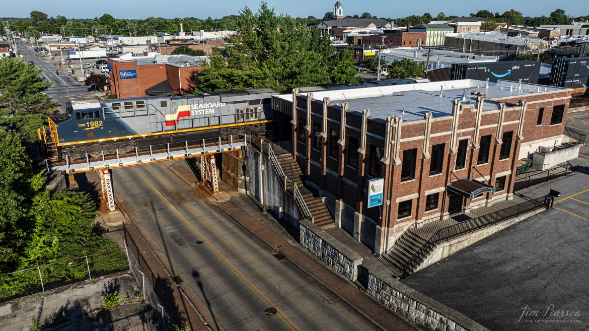 CSX Seaboard System Heritage Locomotive 1982 passes over Arch Street at the old Louisville and Nashville Railroad depot in downtown Madisonville, Kentucky, on June 13th, 2024, as it leads CSX I026 north on the Henderson Subdivision. 

This depot was originally dedicated in 1929 and last saw passenger service about 1968 when L&N built an office at Atkinson Yard in Madisonville and the passenger train service was moved to that location. Currently the station is owned by the city of Madisonville and houses one of the hubs of the Kentucky Innovation Stations, which helps courageous entrepreneurs, creative business founders, high-growth startups, and savvy investors star in their own success stories.

According to Wikipedia: The Seaboard System Railroad, Inc. (reporting mark SBD) was a US Class I railroad that operated from 1982 to 1986.

Since the late 1960s, Seaboard Coast Line Industries had operated the Seaboard Coast Line and its sister railroads, notably the Louisville & Nashville and Clinchfield, as the “Family Lines System”. In 1980, SCLI merged with the Chessie System to create the holding company CSX Corporation; two years later, CSX merged with the Family Lines railroads to create the Seaboard System Railroad.

In 1986, Seaboard renamed itself CSX Transportation, which absorbed the Chessie System’s two major railroads the following year.

Tech Info: DJI Mavic 3 Classic Drone, RAW, 22mm, f/2.8, 1/2000, ISO 140.

#railroad #railroads #train #trains #bestphoto #railroadengines #picturesoftrains #picturesofrailway #bestphotograph #photographyoftrains #trainphotography #JimPearsonPhotography #trendingphoto #csxt #trainsfromadrone