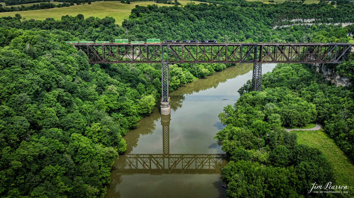 Norfolk Southern intermodal 28C heads northbound across High Bridge on June 8th, 2024, crossing the Kentucky River on the NS CNO&TP First District at Highbridge, Kentucky.

According to Wikipedia: The High Bridge is a railroad bridge crossing the Kentucky River Palisades, that rises approximately 275 feet from the river below and connects Jessamine and Mercer counties in Kentucky. Formally dedicated in 1879, it is the first cantilever bridge constructed in the United States. It has a three-span continuous under-deck truss used by Norfolk Southern Railway to carry trains between Lexington and Danville. It has been designated as a National Historic Civil Engineering Landmark.

In 1851, the Lexington & Danville Railroad, with Julius Adams as chief engineer, retained John A. Roebling to build a railroad suspension bridge across the Kentucky River for a line connecting Lexington and Danville, Kentucky west of the intersection of the Dix and Kentucky rivers. In 1855, the company ran out of money and the project was resumed by Cincinnati Southern Railroad in 1873 following a proposal by C. Shaler Smith for a cantilever design using stone towers designed by John A. Roebling (who designed the Brooklyn Bridge).

The bridge was erected using a cantilever design with a three-span continuous under-deck truss and was opened in 1877 on the Cincinnati Southern Railway. It was 275 feet (84 m) tall and 1,125 feet (343 m) long: the tallest bridge above a navigable waterway in North America and the tallest railroad bridge in the world until the early 20th century. Construction was completed using 3,654,280 pounds of iron at a total cost of $404,373.31. In 1879 President Rutherford B. Hayes and Gen. William Tecumseh Sherman attended the dedication.

After years of heavy railroad use, the bridge was rebuilt by Gustav Lindenthal in 1911. Lindenthal reinforced the foundations and rebuilt the bridge around the original structure. To keep railroad traffic flowing, the track deck was raised by 30 feet during construction and a temporary trestle was constructed. In 1929, an additional set of tracks was built to accommodate increased railroad traffic and the original limestone towers were removed.

Tech Info: DJI Mavic 3 Classic Drone, RAW, 24mm, f/2.8, 1/2000, ISO 160.

#trainphotography #railroadphotography #trains #railways #trainphotographer #railroadphotographer #jimpearsonphotography #NorfolkSouthern #KentuckyTrains