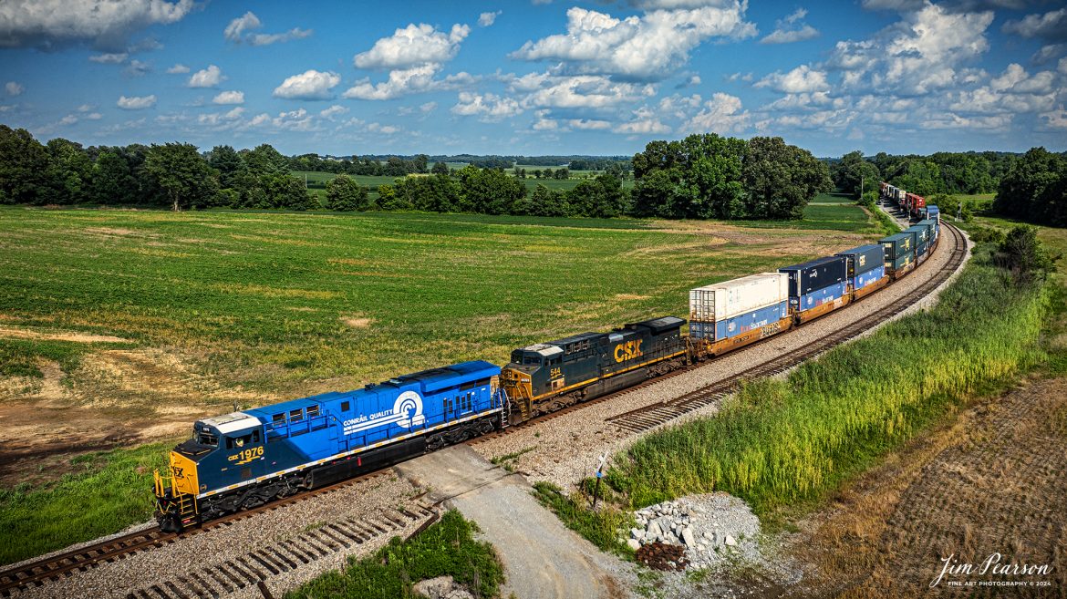 The CSX Conrail Heritage Locomotive leads CSX I026 northbound through the curve at Breton, Ky, on July 10th, 2024, on the CSX Henderson Subdivision as they make their daily run to Chicago, Illinois.

According to a CSX Press Release: July 22, 2023 – CSX has unveiled the fourth locomotive in its series of custom paint designs that honor its heritage railroads. The latest in the series commemorates the Consolidated Rail Corporation, or Conrail, and bears the number 1976, the year the railroad was founded.

CSX and Norfolk Southern acquired and divided most of the Conrail network in 1997. Today, the company continues to exist as a terminal and switching railroad for CSX and NS customers in North Jersey-New York City metro area.

The Conrail paint scheme of a double-lined C inside a large, bold Q was a fixture for many years across the Northeast where the majority of the railroad’s operations were centered. The heritage locomotive design conceived and executed at CSX’s locomotive shop in Waycross, Georgia, recreates the iconic “Conrail Quality” logo and features Conrail blue on the rear two-thirds of the engine, then transitions to the current CSX colors and design on the cab portion of the unit.

CSX 1976 and other locomotives in the heritage series will be placed into revenue service and travel CSX’s 20,000 rail network, reinforcing employee pride in the history of the railroad that continues to move the nation’s economy with safe, reliable and sustainable rail-based transportation services.

Tech Info: DJI Mavic 3 Classic Drone, RAW, 22mm, f/2.8, 1/2000, ISO 100.

#railroad #railroads #train #trains #bestphoto #railroadengines #picturesoftrains #picturesofrailway #bestphotograph #photographyoftrains #trainphotography #JimPearsonPhotography #trendingphoto