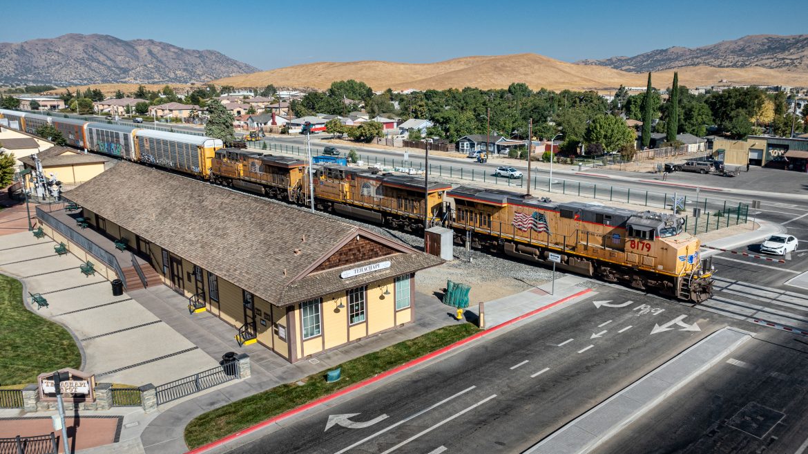 September 18th, 2024, Union Pacific 8179 leads a eastbound autorack past the museum depot in downtown Tehachapi, California, on the Union Pacific Mojave Subdivision.

According to Wikipedia: The Tehachapi Railroad Depot was a railroad station in Tehachapi, California. The Southern Pacific Railroad built the line through the area in 1876. The depot was built in 1904 after the original station building was destroyed in a fire. the railroad founded the town of Tehachapi and drew the residents of nearby Tehichipa to the new settlement. The depot served a significant section of railroad, as it was located near the Tehachapi Loop and was one of the most active rural stations during World War II. The station later served as a warehouse and a railroad office.

This railroad that crossed the Tehachapi Summit and came through Tehachapi was the second transcontinental railroad. The museum has a collection of old railroad tools and signals, photos and newspaper articles, lanterns, and dining cart china. Much of this came from the family of Bill Stokoe, a retired railroad worker who passed away in 1999.

In 2008, the depot burned down; it was rebuilt in 2009 and now serves as the Tehachapi Depot Railroad Museum with historic railroad artifacts.

The original depot was added to the National Register of Historic Places on October 20, 1999. Although the original depot no longer exists, it remains on the National Register.

Tech Info: DJI Mavic 3 Classic Drone, RAW, 24mm, f/2.8, 1/2000, ISO 110.

#railroad #railroads #train, #trains #railway #railway #steamtrains #railtransport #railroadengines #picturesoftrains #picturesofrailways #besttrainphotograph #bestphoto #photographyoftrains #bestsoldpicture #JimPearsonPhotography #trainsfromtheair #trainsfromadrone #Tehachapi