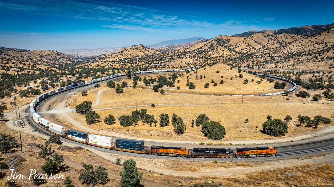 September 18th, 2024, BNSF 8057, NS 8068 and BNSF 5177 lead an eastbound train through the famous Tehachapi Loop on the Union Pacific Mojave Subdivision at Keene, California.

I’m thankful that I had and brought my drone on this trip as access to trackside at the loop has been cut off! I was last here 7 years ago and then you could get to where you could shoot trackside, but now there’s viewing platform about ¾ mile away. Being able to fly the drone allowed me many spectacular views that I’ve never been able to get in the past.

According to their website: The Tehachapi Loop is a 3,779-foot-long (0.72 mi; 1.15 km) spiral, or helix, on the Union Pacific Railroad Mojave Subdivision through Tehachapi Pass, of the Tehachapi Mountains in Kern County, south-central California. The line connects Bakersfield and the San Joaquin Valley to Mojave in the Mojave Desert.
Rising at a steady two-percent grade, the track gains 77 feet (23 m) in elevation and makes a 1,210-foot-diameter (370 m) circle. Any train that is more than 3,800 feet (1,200 m) long—about 56 boxcars—passes over itself going around the loop. At the bottom of the loop, the track passes through Tunnel 9, the ninth tunnel built as the railroad was extended from Bakersfield.

The line averages about 36 freight trains each day. Passenger trains such as Amtrak's San Joaquin are banned from the loop, although the Coast Starlight can use it as a detour. ts frequent trains and scenic setting make the Tehachapi Loop popular with railfans. In 1998, it was named a National Historic Civil Engineering Landmark. It is also designated as California Historical Landmark #508.

One of the engineering feats of its day, the Loop was built by Southern Pacific Railroad to ease the grade over Tehachapi Pass. Construction began in 1874, and the line opened in 1876.

Tech Info: DJI Mavic 3 Classic Drone, RAW, 24mm, f/2.8, 1/2500, ISO 100.

#railroad #railroads #train, #trains #railway #railway #steamtrains #railtransport #railroadengines #picturesoftrains #picturesofrailways #besttrainphotograph #bestphoto #photographyoftrains #bestsoldpicture #JimPearsonPhotography #trainsfromtheair #trainsfromadrone #TehachapiLoop