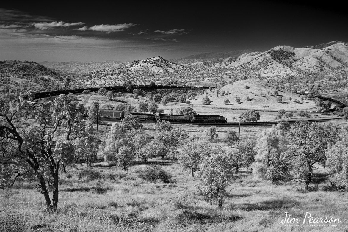 September 18th, 2024, In this Saturday's Infrared photo  I caught BNSF 7904, 7853 and 2167 leading an eastbound train through the famous Tehachapi Loop on the Union Pacific Mojave Subdivision at Keene,  California.

According to Wikipedia: The Tehachapi Loop is a 3,779-foot-long (0.72 mi; 1.15 km) spiral, or helix, on the Union Pacific Railroad Mojave Subdivision through Tehachapi Pass, of the Tehachapi Mountains in Kern County, south-central California. The line connects Bakersfield and the San Joaquin Valley to Mojave in the Mojave Desert.

Rising at a steady two-percent grade, the track gains 77 feet (23 m) in elevation and makes a 1,210-foot-diameter (370 m) circle. Any train that is more than 3,800 feet (1,200 m) long—about 56 boxcars—passes over itself going around the loop. At the bottom of the loop, the track passes through Tunnel 9, the ninth tunnel built as the railroad was extended from Bakersfield.

The line averages about 36 freight trains each day. Passenger trains such as Amtrak's San Joaquin are banned from the loop, although the Coast Starlight can use it as a detour. Its frequent trains and scenic setting make the Tehachapi Loop popular with railfans. In 1998, it was named a National Historic Civil Engineering Landmark. It is also designated as California Historical Landmark #508.

One of the engineering feats of its day, the Loop was built by Southern Pacific Railroad to ease the grade over Tehachapi Pass. Construction began in 1874, and the line opened in 1876.

Tech Info: Fuji XT1 converted to Infrared, RAW, Nikon 24-70, @24mm, f/4, 1/1000, ISO 100.

#railroad #railroads #train, #trains #railway #railway #steamtrains #railtransport #railroadengines #picturesoftrains #picturesofrailways #besttrainphotograph #bestphoto #photographyoftrains #bestsoldpicture #JimPearsonPhotography #Infrared #TehachapiLoop