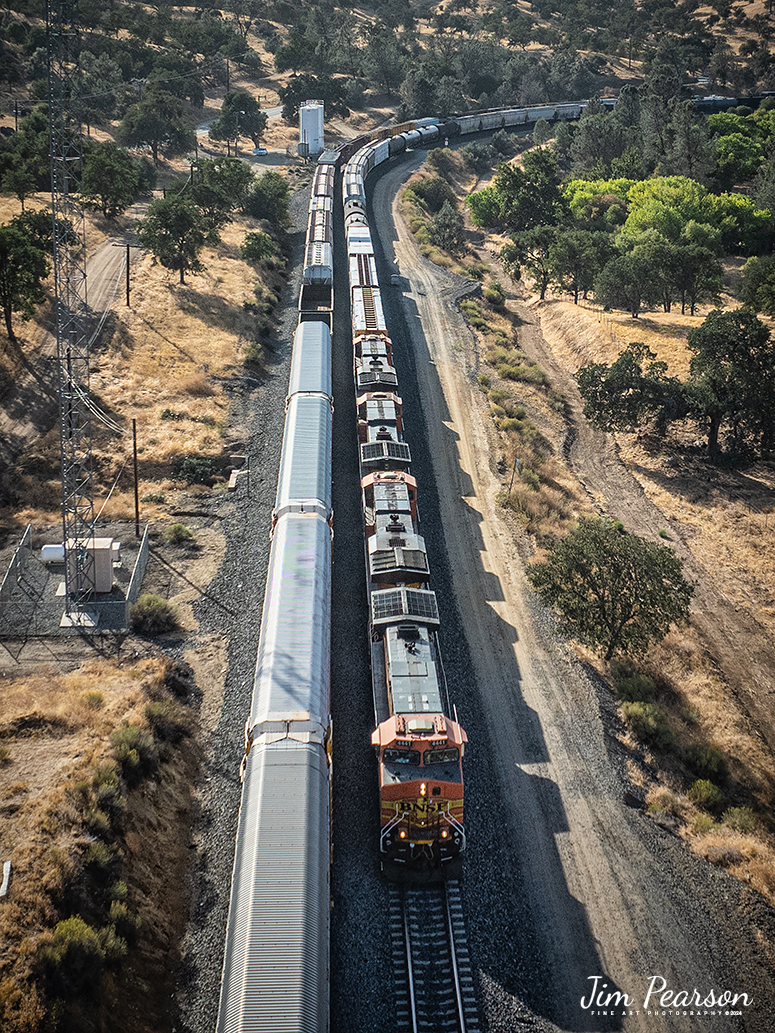 September 18th, 2024, A BNSF westbound train passes another westbound that is waiting to continue its move east through Tehachapi Loop on the Union Pacific Mojave Subdivision at Keene, California.



According to Wikipedia: The Tehachapi Loop is a 3,779-foot-long (0.72 mi; 1.15 km) spiral, or helix, on the Union Pacific Railroad Mojave Subdivision through Tehachapi Pass, of the Tehachapi Mountains in Kern County, south-central California. The line connects Bakersfield and the San Joaquin Valley to Mojave in the Mojave Desert.



Rising at a steady two-percent grade, the track gains 77 feet (23 m) in elevation and makes a 1,210-foot-diameter (370 m) circle. Any train that is more than 3,800 feet (1,200 m) long—about 56 boxcars—passes over itself going around the loop. At the bottom of the loop, the track passes through Tunnel 9, the ninth tunnel built as the railroad was extended from Bakersfield.



The line averages about 36 freight trains each day. Passenger trains such as Amtrak's San Joaquin are banned from the loop, although the Coast Starlight can use it as a detour. Its frequent trains and scenic setting make the Tehachapi Loop popular with railfans. In 1998, it was named a National Historic Civil Engineering Landmark. It is also designated as California Historical Landmark #508.


One of the engineering feats of its day, the Loop was built by Southern Pacific Railroad to ease the grade over Tehachapi Pass. Construction began in 1874, and the line opened in 1876.



Tech Info: DJI Mavic 3 Classic Drone, RAW, 24mm, f/2.8, 1/2500, ISO 160.



#railroad #railroads #train, #trains #railway #railway #steamtrains #railtransport #railroadengines #picturesoftrains #picturesofrailways #besttrainphotograph #bestphoto #photographyoftrains #bestsoldpicture #JimPearsonPhotography #trainsfromtheair #trainsfromadrone #TehachapiLoop