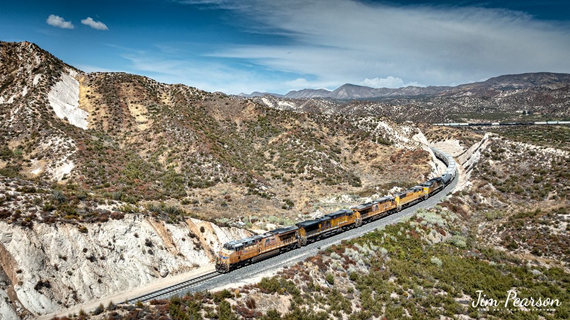 A Union Pacific freight makes its way west down the Cajon Pass as it approaches the Mormon Rocks area in Cajon Pass, California on September 20th, 2024.

According to Wikipedia: Cajon Pass is a mountain pass between the San Bernardino Mountains to the east and the San Gabriel Mountains to the west in Southern California. Created by the movements of the San Andreas Fault, it has an elevation of 3,777 ft (1,151 m). Located in the Mojave Desert, the pass is an important link from the Greater San Bernardino Area to the Victor Valley, and northeast to Las Vegas. The Cajon Pass area is on the Pacific Crest Trail.

Cajon Pass is at the head of Horsethief Canyon, traversed by California State Route 138 (SR 138) and railroad tracks owned by BNSF Railway and Union Pacific Railroad. Improvements in 1972 reduced the railroad's maximum elevation from about 3,829 to 3,777 feet while reducing curvature. Interstate 15 does not traverse Cajon Pass, but rather the nearby Cajon Summit. The entire area, Cajon Pass and Cajon Summit, is often referred to as Cajon Pass, but a distinction is made between Cajon Pass and Cajon Summit.

The California Southern Railroad, a subsidiary of the Atchison, Topeka and Santa Fe Railway, was the first railroad through Cajon Pass. The line through the pass was built in the early 1880s to connect the present-day cities of Barstow and San Diego. Today the Union Pacific Railroad and BNSF Railway (the successor to the Santa Fe) use the pass to reach Los Angeles and San Bernardino as part of the Southern Transcon. Due to the many trains, scenery and easy access, it is a popular location for railfans, and many photographs of trains on Cajon Pass appear in books and magazines.

The Union Pacific Railroad owns one track through the pass, on the previous Southern Pacific Railroad Palmdale cutoff, opened in 1967. The BNSF Railway owns two tracks and began to operate a third main track in the summer of 2008. The railroads share track rights through the pass ever since the Union Pacific gained track rights on the Santa Fe portion negotiated under the original Los Angeles and Salt Lake Railroad. 

Tech Info: DJI Mavic 3 Classic Drone, RAW, 24mm, f/2.8, 1/2000, ISO 100.

#railroad #railroads #train, #trains #railway #railway #steamtrains #railtransport #railroadengines #picturesoftrains #picturesofrailways #besttrainphotograph #bestphoto #photographyoftrains #bestsoldpicture #JimPearsonPhotography #trainsfromtheair #trainsfromadrone #CajonPass