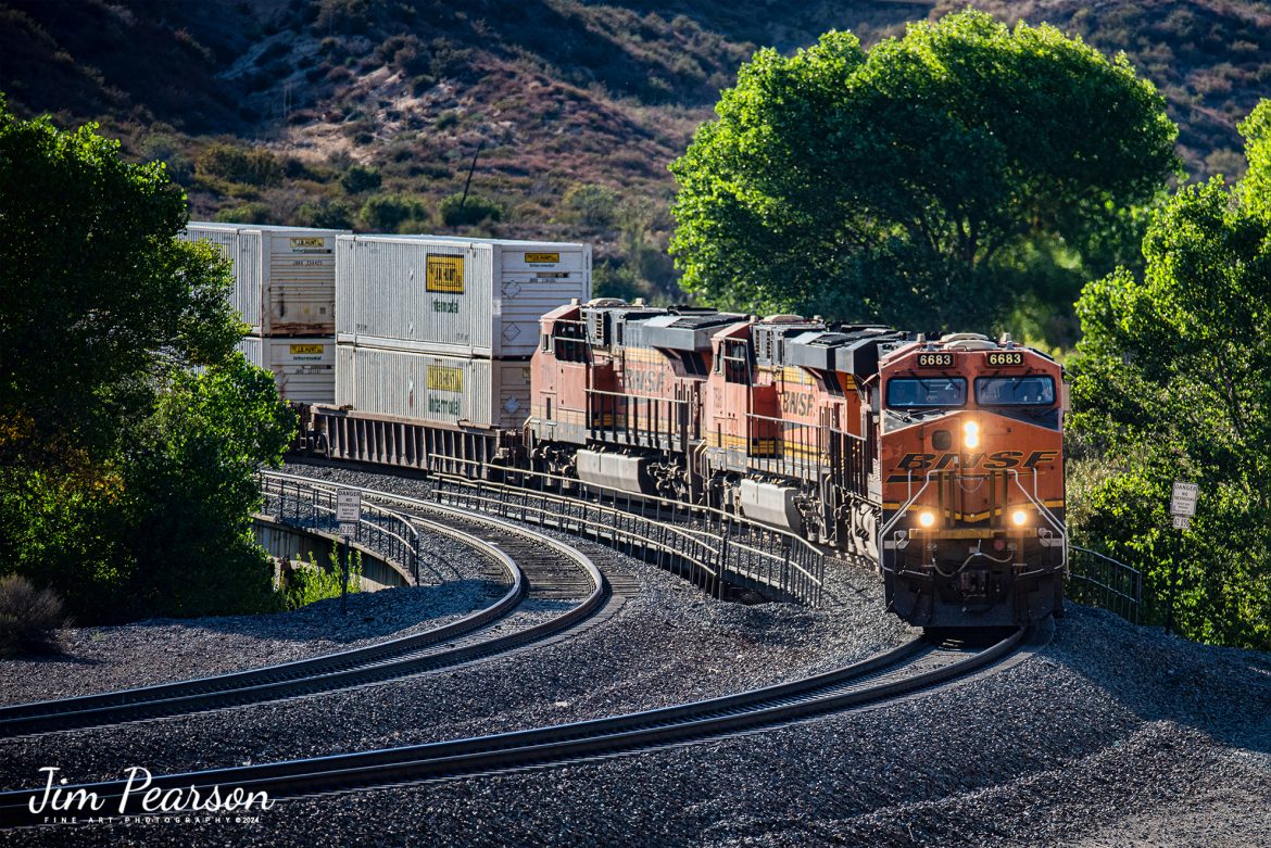 BNSF 6673 leads an eastbound intermodal as it rounds a curve coming down hill in the Cajon Pass at Cajon, California on the BNSF Cajon Subdivision, on September 24th, 2024. 

According to Wikipedia: Cajon Pass is a mountain pass between the San Bernardino Mountains to the east and the San Gabriel Mountains to the west in Southern California. Created by the movements of the San Andreas Fault, it has an elevation of 3,777 ft (1,151 m). Located in the Mojave Desert, the pass is an important link from the Greater San Bernardino Area to the Victor Valley, and northeast to Las Vegas. The Cajon Pass area is on the Pacific Crest Trail.

Cajon Pass is at the head of Horsethief Canyon, traversed by California State Route 138 (SR 138) and railroad tracks owned by BNSF Railway and Union Pacific Railroad. Improvements in 1972 reduced the railroad's maximum elevation from about 3,829 to 3,777 feet while reducing curvature. Interstate 15 does not traverse Cajon Pass, but rather the nearby Cajon Summit. The entire area, Cajon Pass and Cajon Summit, is often referred to as Cajon Pass, but a distinction is made between Cajon Pass and Cajon Summit.

The California Southern Railroad, a subsidiary of the Atchison, Topeka and Santa Fe Railway, was the first railroad through Cajon Pass. The line through the pass was built in the early 1880s to connect the present-day cities of Barstow and San Diego. Today the Union Pacific Railroad and BNSF Railway (the successor to the Santa Fe) use the pass to reach Los Angeles and San Bernardino as part of the Southern Transcon. Due to the many trains, scenery and easy access, it is a popular location for railfans, and many photographs of trains on Cajon Pass appear in books and magazines.

The Union Pacific Railroad owns one track through the pass, on the previous Southern Pacific Railroad Palmdale cutoff, opened in 1967. The BNSF Railway owns two tracks and began to operate a third main track in the summer of 2008. The railroads share track rights through the pass ever since the Union Pacific gained track rights on the Santa Fe portion negotiated under the original Los Angeles and Salt Lake Railroad. 

Tech Info: Nikon D810, RAW, Nikon 70-300 @ 220mm, f/5.6, 1/800, ISO 280.

#railroad #railroads #train, #trains #railway #railway #steamtrains #railtransport #railroadengines #picturesoftrains #picturesofrailways #besttrainphotograph #bestphoto #photographyoftrains #bestsoldpicture #JimPearsonPhotography #trainsfromtheair #CajonPass #bnsf