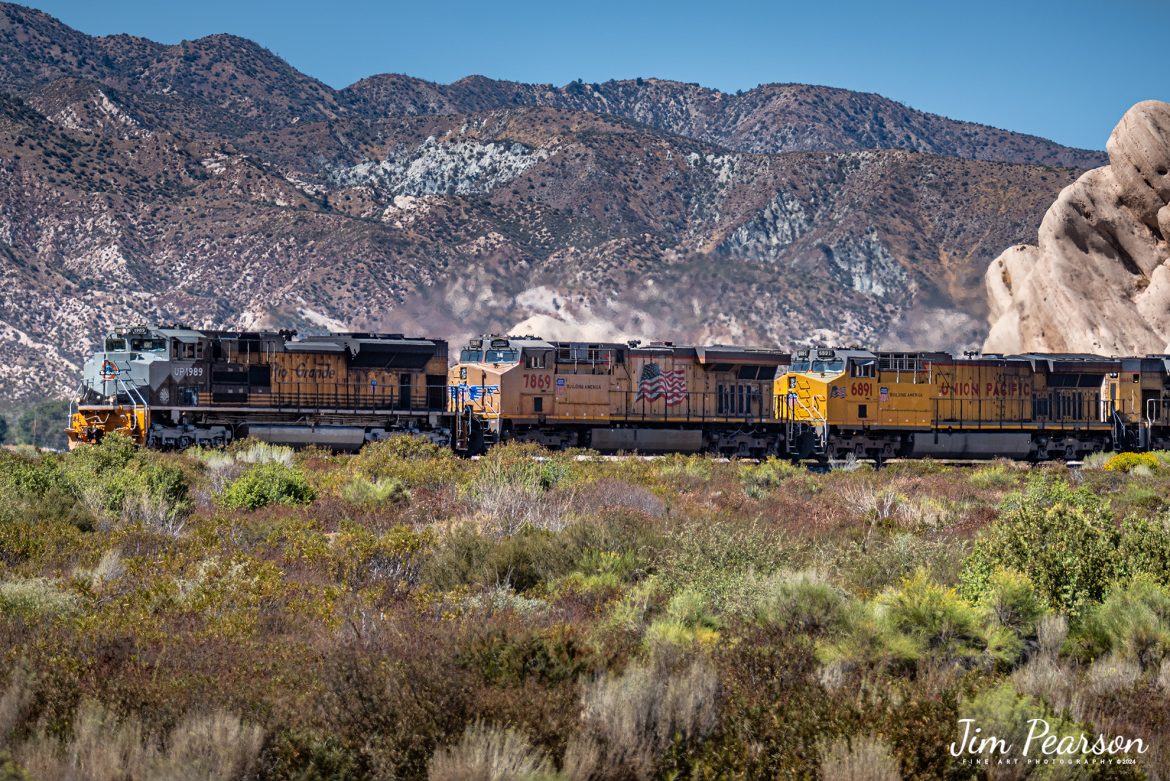 I didn’t have a clue that Union Pacific 1989, Rio Grande Heritage Unit, was leading this eastbound freight until it appeared from behind Mormon Rocks in the Cajon Pass on September 24th, 2024. 

I was set up on the BNSF double track below the UP line as there was another BNSF train approaching there. I had to scramble and switch from the video I was planning to shoot and pull up my D810 with the 70-300mm on it to grab this and a couple other shots before it disappeared behind brush and hillside. I would have much rather had it coming out of Mormon Rocks, but it wasn’t meant to be, I guess.

According to the Union Pacific Website: Incorporating historic colors and graphic elements of the Denver & Rio Grande Western Railroad, No. 1989 pays tribute to the men and women of the railroad who "went everywhere the hard way."

Founded by Gen. William J. Palmer, a Union veteran of the Civil War, the Rio Grande started building a narrow-gauge line south from Denver in 1871 toward Mexico. At its peak mileage in 1917, the Rio Grande was operating nearly 6,000 miles of track.

On-line coal, bridge traffic with friendly connections, and the opening of the 6.2-mile Moffat Tunnel in 1928 that dramatically shortened its Denver-Salt Lake Route, the Rio Grande became known for its competitive spirit and mountain scenery. The "Grand Canyon of the Arkansas River," known as the Royal Gorge, was one of the highlights on the route through the Rockies when The Denver & Rio Grande was known as the Scenic Line of the World.

Rio Grande Industries purchased Southern Pacific Lines on Sept. 12, 1988, and combined the systems on Oct. 13, 1988, operating under the name Southern Pacific. Union Pacific and Southern Pacific merged on Sept. 11, 1996.

According to Wikipedia: The Union Pacific Railroad owns one track through the pass, on the previous Southern Pacific Railroad Palmdale cutoff, opened in 1967. The BNSF Railway owns two tracks and began to operate a third main track in the summer of 2008. The railroads share track rights through the pass ever since the Union Pacific gained track rights on the Santa Fe portion negotiated under the original Los Angeles and Salt Lake Railroad. 

Tech Info: Nikon D810, RAW, Nikon 70-300 @ 175mm, f/5.3, 1/800, ISO 100.

#railroad #railroads #train, #trains #railway #railway #steamtrains #railtransport #railroadengines #picturesoftrains #picturesofrailways #besttrainphotograph #bestphoto #photographyoftrains #bestsoldpicture #JimPearsonPhotography #trainsfromtheair #CajonPass #unionpacific