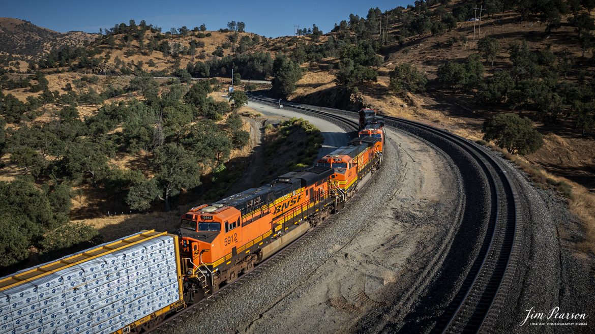 September 18th, 2024, BNSF 4441 leads an northbound  freight train after they skirt around tunnel 10 from Tehachapi Loop on the Union Pacific Mojave Subdivision at, Woodford, California.

According to Wikipedia: The Tehachapi Loop is a 3,779-foot-long (0.72 mi; 1.15 km) spiral, or helix, on the Union Pacific Railroad Mojave Subdivision through Tehachapi Pass, of the Tehachapi Mountains in Kern County, south-central California. The line connects Bakersfield and the San Joaquin Valley to Mojave in the Mojave Desert.

Rising at a steady two-percent grade, the track gains 77 feet (23 m) in elevation and makes a 1,210-foot-diameter (370 m) circle. Any train that is more than 3,800 feet (1,200 m) long—about 56 boxcars—passes over itself going around the loop. At the bottom of the loop, the track passes through Tunnel 9, the ninth tunnel built as the railroad was extended from Bakersfield.

The line averages about 36 freight trains each day. Passenger trains such as Amtrak's San Joaquin are banned from the loop, although the Coast Starlight can use it as a detour. Its frequent trains and scenic setting make the Tehachapi Loop popular with railfans. In 1998, it was named a National Historic Civil Engineering Landmark. It is also designated as California Historical Landmark #508.

One of the engineering feats of its day, the Loop was built by Southern Pacific Railroad to ease the grade over Tehachapi Pass. Construction began in 1874, and the line opened in 1876.

Tech Info: DJI Mavic 3 Classic Drone, RAW, 24mm, f/2.8, 1/2500, ISO 150.

#railroad #railroads #train, #trains #railway #railway #steamtrains #railtransport #railroadengines #picturesoftrains #picturesofrailways #besttrainphotograph #bestphoto #photographyoftrains #bestsoldpicture #JimPearsonPhotography #trainsfromtheair #trainsfromadrone