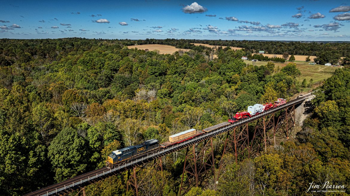 CSXT 85 leads S991 as they cross the Gum Lick Trestle on a depressed flatbed at Kelly, Kentucky with an oversized load heading south on October 16th, 2024, on the CSX Henderson Subdivision. The load is traveling on KRL 204041, a Schnabel car with Red and Ready KRL 073 caboose trailing.  
According to Wikipedia: A Schnabel car or Schnabel wagon is a specialized type of railroad freight car. It is designed to carry heavy and oversized loads in such a way that the load makes up part of the car. The load is suspended between the two ends of the cars by lifting arms; the lifting arms are connected to an assembly of span bolsters that distribute the weight of the load and the lifting arm over many wheels.

When a Schnabel car is empty, the two lifting arms are connected to one another and the car can usually operate at normal freight train speeds. Some Schnabel cars include hydraulic equipment that will either lift or horizontally shift the load while in transit (at very low speeds) to clear obstructions along the car's route. 

That is the case with this car as there was a crew on the caboose that shifted the load whenever necessary on meets or areas with close clearance. It was traveling at 25 mph on the mains and much slower through turnouts and switches.

Tech Info: DJI Mavic 3 Classic Drone, RAW, 22mm, f/2.8, 1/2500, ISO 140.

#trainphotography #jimpearsonphotography #trending #csxt #bestsoldphotos