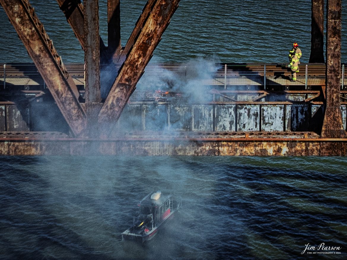 Members of the Henderson Fire Department work on putting out a tie fire on the bridge that spans the Ohio River on the CSX Henderson Subdivision at Henderson, Kentucky as a fire boat works from below. Several ties were involved in the fire on the afternoon of October 26th, 2024, and fortunately except for the ties, the bridge is made out of steel.

The fire did disrupt traffic on the CSX Henderson Subdivision for a couple hours and while CSX M648 did make it across after being delayed about 30 minutes and after the ties were first put out, afterwards the ties reignited and delayed hot intermodal I025 on the Evansville, IN, side of the river for almost two hours, till the ties were completely extinguished. I’ll be posting shots with M648 with the CE&I heritage unit leading across the bridge this afternoon, so stay tuned!

Tech Info: DJI Mavic 3 Classic Drone, RAW, 24mm, f/5, 1/2000, ISO 110.

#picturesofrailways #besttrainphotograph #bestphoto #photographyoftrains #bestsoldpicture #JimPearsonPhotography