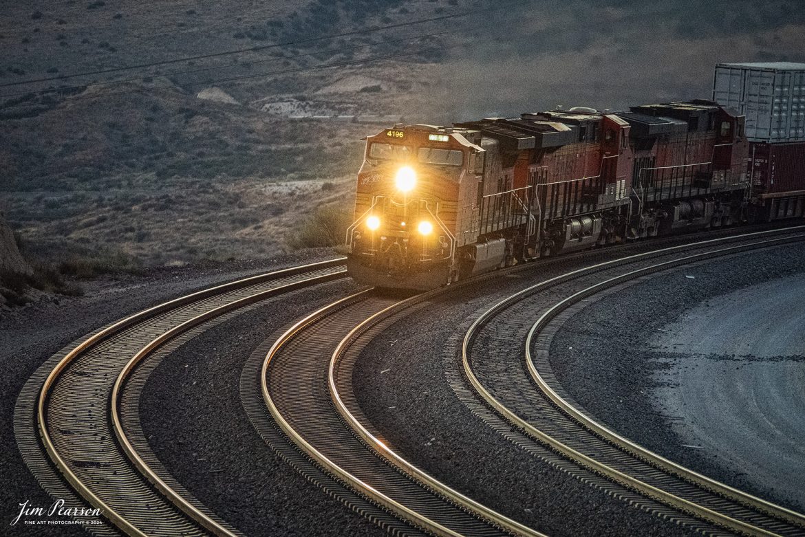 September 19th, 2024, BNSF 4196 leads a stack train as they approach the Summit of Cajon Pass in southern California and the BNSF Cajon Subdivision at dusk.

According to Wikipedia: Cajon Pass is a mountain pass between the San Bernardino Mountains to the east and the San Gabriel Mountains to the west in Southern California. Created by the movements of the San Andreas Fault, it has an elevation of 3,777 ft (1,151 m). Located in the Mojave Desert, the pass is an important link from the Greater San Bernardino Area to the Victor Valley, and northeast to Las Vegas. The Cajon Pass area is on the Pacific Crest Trail.

Cajon Pass is at the head of Horsethief Canyon, traversed by California State Route 138 (SR 138) and railroad tracks owned by BNSF Railway and Union Pacific Railroad. Improvements in 1972 reduced the railroad's maximum elevation from about 3,829 to 3,777 feet while reducing curvature. Interstate 15 does not traverse Cajon Pass, but rather the nearby Cajon Summit. The entire area, Cajon Pass and Cajon Summit, is often referred to as Cajon Pass, but a distinction is made between Cajon Pass and Cajon Summit.

The California Southern Railroad, a subsidiary of the Atchison, Topeka and Santa Fe Railway, was the first railroad through Cajon Pass. The line through the pass was built in the early 1880s to connect the present-day cities of Barstow and San Diego. Today the Union Pacific Railroad and BNSF Railway (the successor to the Santa Fe) use the pass to reach Los Angeles and San Bernardino as part of the Southern Transcon. Due to the many trains, scenery and easy access, it is a popular location for railfans, and many photographs of trains on Cajon Pass appear in books and magazines.

The Union Pacific Railroad owns one track through the pass, on the previous Southern Pacific Railroad Palmdale cutoff, opened in 1967. The BNSF Railway owns two tracks and began to operate a third main track in the summer of 2008. The railroads share track rights through the pass ever since the Union Pacific gained track rights on the Santa Fe portion negotiated under the original Los Angeles and Salt Lake Railroad. 

Tech Info: Nikon D810, RAW, Sigma 150-600 @240mm, f/5.6, 1/250, ISO 12800.

#photographyoftrains #trainphotography #JimPearsonPhotography #trendingphoto