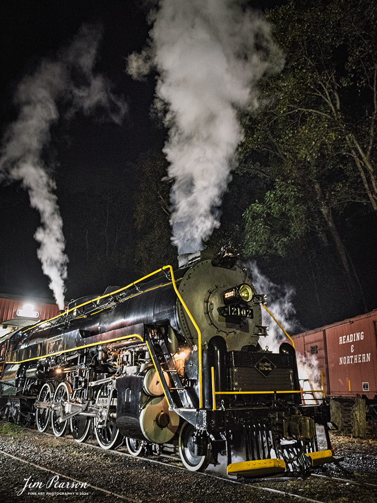 70300Reading Blue Mountain & Northern Railroad steam locomotive 2102 sits outside the engine house as dawn begins at Port Clinton, Pennsylvania on October 5th, 2024, as it waits to begin its first day of the year of pulling Fall Foliage Excursions.

According to their website: The Reading Company T-1 class #2102 was built in the Reading’s own locomotive shops in 1945. With drivers of 70” diameter, it weighs 404 tons, and its tender holds up to 26 tons of coal, and up to 19,000 gallons of water. After the Reading Steam era was over, the Reading Company used 2102 for the Reading Rambles on several different excursions. The 2102 has had many different owners since it was retired by the Reading Railroad. It is one of only four to survive. The other remaining locomotives are the 2100, 2101, and 2124.

The Blue Mountain and Reading Railroad purchased the 2102 in 1987, and it ran on the Temple to South Hamburg line into the early 1990’s. Once the Blue Mountain and Reading Railroad became the Reading Blue Mountain & Northern, the 2102 ran over Reading & Northern’s rails for a short time before it was removed from service in the early 1990’s. 

In 2022, steam locomotive 2102 reentered service on the Reading & Northern. The locomotive has been used actively to pull both passenger excursions and revenue freight trains.

Tech Info: Nikon D810, RAW, Nikon 24-70 @ 26mm, f/2.8, 1/15, ISO 4500.

#railroad #railroads #train, #trains #railway #railway #steamtrains #railtransport #railroadengines #picturesoftrains #picturesofrailways #besttrainphotograph #bestphoto #photographyoftrains #bestsoldpicture #JimPearsonPhotography #RBNRR