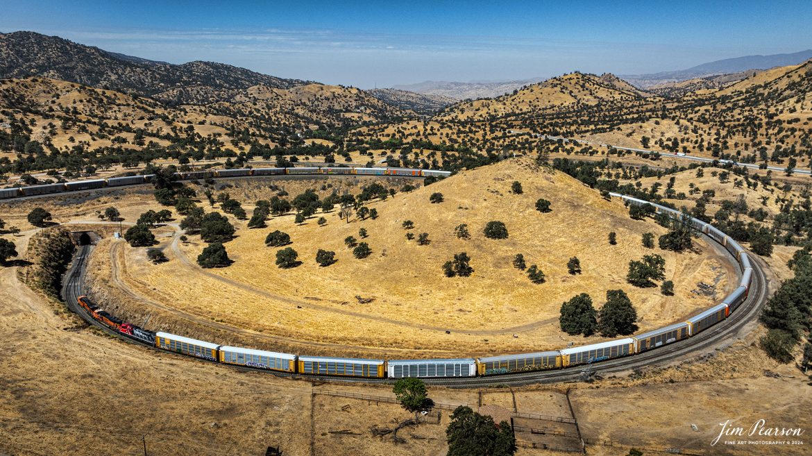 September 18th, 2024, BNSF 7115, 9128 and Ferromex 4050 lead an northbound train through Tehachapi Loop on the Union Pacific Mojave Subdivision at Keene, California.

According to Wikipedia: The Tehachapi Loop is a 3,779-foot-long (0.72 mi; 1.15 km) spiral, or helix, on the Union Pacific Railroad Mojave Subdivision through Tehachapi Pass, of the Tehachapi Mountains in Kern County, south-central California. The line connects Bakersfield and the San Joaquin Valley to Mojave in the Mojave Desert.

Rising at a steady two-percent grade, the track gains 77 feet (23 m) in elevation and makes a 1,210-foot-diameter (370 m) circle. Any train that is more than 3,800 feet (1,200 m) long—about 56 boxcars—passes over itself going around the loop. At the bottom of the loop, the track passes through Tunnel 9, the ninth tunnel built as the railroad was extended from Bakersfield.

The line averages about 36 freight trains each day. Passenger trains such as Amtrak's San Joaquin are banned from the loop, although the Coast Starlight can use it as a detour. Its frequent trains and scenic setting make the Tehachapi Loop popular with railfans. In 1998, it was named a National Historic Civil Engineering Landmark. It is also designated as California Historical Landmark #508.

One of the engineering feats of its day, the Loop was built by Southern Pacific Railroad to ease the grade over Tehachapi Pass. Construction began in 1874, and the line opened in 1876.

Tech Info: DJI Mavic 3 Classic Drone, RAW, 24mm, f/2.8, 1/2500, ISO 100.

#railroad #railroads #train, #trains #railway #railway #steamtrains #railtransport #railroadengines #picturesoftrains #picturesofrailways #besttrainphotograph #bestphoto #photographyoftrains #bestsoldpicture #JimPearsonPhotography #trainsfromtheair #trainsfromadrone #TehachapiLoop