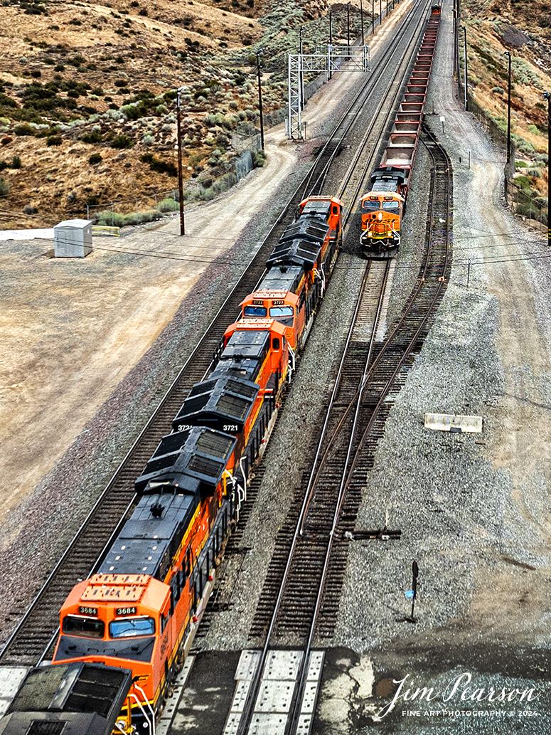 September 20th, 2024, A BNSF freight and a BNSF rock train pass each other at the Summit of Cajon Pass in southern California and the BNSF Cajon Subdivision.

According to Wikipedia: Cajon Pass is a mountain pass between the San Bernardino Mountains to the east and the San Gabriel Mountains to the west in Southern California. Created by the movements of the San Andreas Fault, it has an elevation of 3,777 ft (1,151 m). Located in the Mojave Desert, the pass is an important link from the Greater San Bernardino Area to the Victor Valley, and northeast to Las Vegas. The Cajon Pass area is on the Pacific Crest Trail.

Cajon Pass is at the head of Horsethief Canyon, traversed by California State Route 138 (SR 138) and railroad tracks owned by BNSF Railway and Union Pacific Railroad. Improvements in 1972 reduced the railroad's maximum elevation from about 3,829 to 3,777 feet while reducing curvature. Interstate 15 does not traverse Cajon Pass, but rather the nearby Cajon Summit. The entire area, Cajon Pass and Cajon Summit, is often referred to as Cajon Pass, but a distinction is made between Cajon Pass and Cajon Summit.

The California Southern Railroad, a subsidiary of the Atchison, Topeka and Santa Fe Railway, was the first railroad through Cajon Pass. The line through the pass was built in the early 1880s to connect the present-day cities of Barstow and San Diego. Today the Union Pacific Railroad and BNSF Railway (the successor to the Santa Fe) use the pass to reach Los Angeles and San Bernardino as part of the Southern Transcon. Due to the many trains, scenery and easy access, it is a popular location for railfans, and many photographs of trains on Cajon Pass appear in books and magazines.

Tech Info: DJI Mavic 3 Classic Drone, RAW, 24mm, f/2.8, 1/2000, ISO 110.

#railroad #railroads #train, #trains #railway #railway #steamtrains #railtransport #railroadengines #picturesoftrains #picturesofrailways #besttrainphotograph #bestphoto #photographyoftrains #bestsoldpicture #JimPearsonPhotography #trainsfromtheair #trainsfromadrone #CajonPass