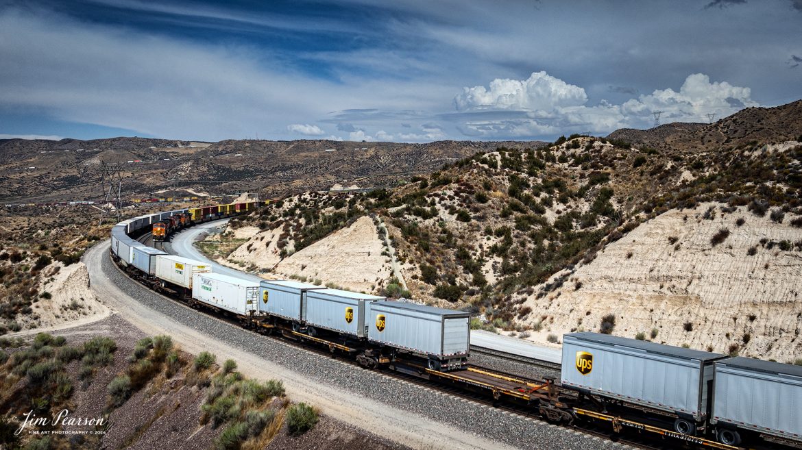 September 20th, 2024, Two BNSF trains pass each other at the at the Summit of Cajon Pass in southern California and the BNSF Cajon Subdivision.

According to Wikipedia: Cajon Pass is a mountain pass between the San Bernardino Mountains to the east and the San Gabriel Mountains to the west in Southern California. Created by the movements of the San Andreas Fault, it has an elevation of 3,777 ft (1,151 m). Located in the Mojave Desert, the pass is an important link from the Greater San Bernardino Area to the Victor Valley, and northeast to Las Vegas. The Cajon Pass area is on the Pacific Crest Trail.

Cajon Pass is at the head of Horsethief Canyon, traversed by California State Route 138 (SR 138) and railroad tracks owned by BNSF Railway and Union Pacific Railroad. Improvements in 1972 reduced the railroad's maximum elevation from about 3,829 to 3,777 feet while reducing curvature. Interstate 15 does not traverse Cajon Pass, but rather the nearby Cajon Summit. The entire area, Cajon Pass and Cajon Summit, is often referred to as Cajon Pass, but a distinction is made between Cajon Pass and Cajon Summit.

The California Southern Railroad, a subsidiary of the Atchison, Topeka and Santa Fe Railway, was the first railroad through Cajon Pass. The line through the pass was built in the early 1880s to connect the present-day cities of Barstow and San Diego. Today the Union Pacific Railroad and BNSF Railway (the successor to the Santa Fe) use the pass to reach Los Angeles and San Bernardino as part of the Southern Transcon. Due to the many trains, scenery and easy access, it is a popular location for railfans, and many photographs of trains on Cajon Pass appear in books and magazines.

Tech Info: DJI Mavic 3 Classic Drone, RAW, 24mm, f/2.8, 1/2500, ISO 100.

#railroad #railroads #train, #trains #railway #railway #steamtrains #railtransport #railroadengines #picturesoftrains #picturesofrailways #besttrainphotograph #bestphoto #photographyoftrains #bestsoldpicture #JimPearsonPhotography #trainsfromtheair #trainsfromadrone #CajonPass