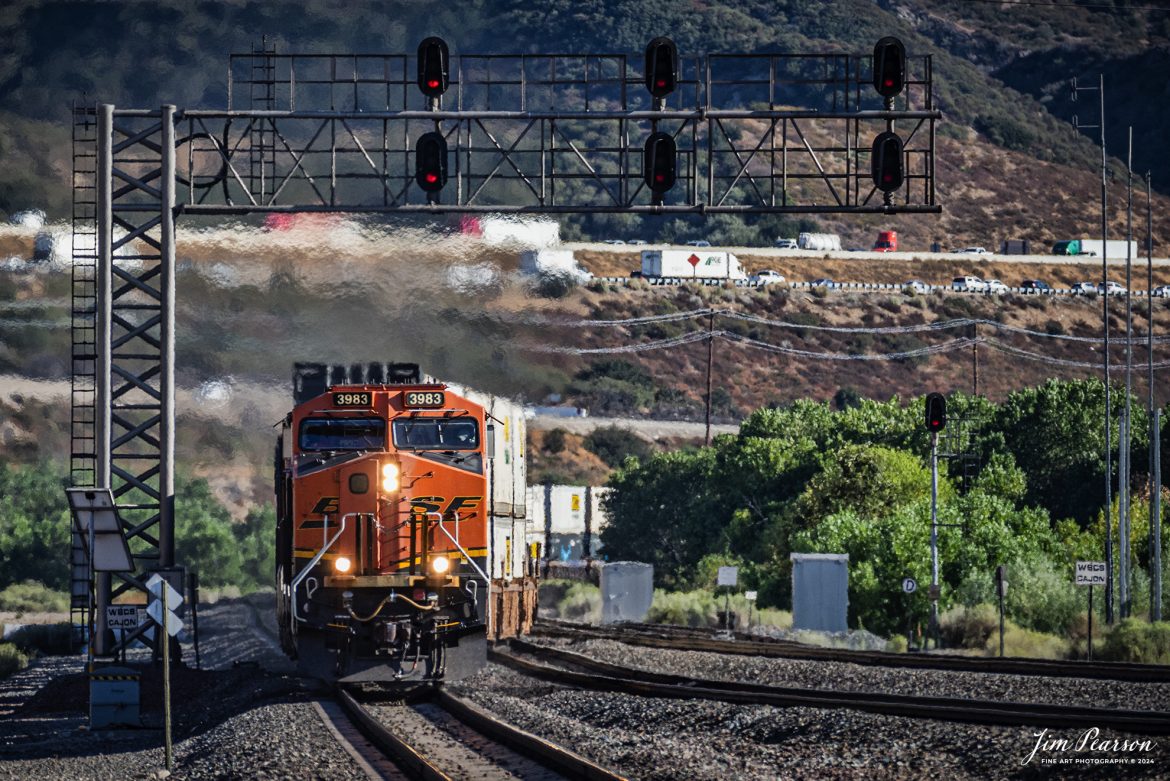 BNSF 3983 leads an intermodal as it passes under the signal bridge at Cajon in the Cajon Pass in southern California on the BNSF Cajon Subdivision, on September 24th, 2024 as it climbs the grade toward Barstow, CA. 

According to Wikipedia: Cajon Pass is a mountain pass between the San Bernardino Mountains to the east and the San Gabriel Mountains to the west in Southern California. Created by the movements of the San Andreas Fault, it has an elevation of 3,777 ft (1,151 m). Located in the Mojave Desert, the pass is an important link from the Greater San Bernardino Area to the Victor Valley, and northeast to Las Vegas. The Cajon Pass area is on the Pacific Crest Trail.

Cajon Pass is at the head of Horsethief Canyon, traversed by California State Route 138 (SR 138) and railroad tracks owned by BNSF Railway and Union Pacific Railroad. Improvements in 1972 reduced the railroad's maximum elevation from about 3,829 to 3,777 feet while reducing curvature. Interstate 15 does not traverse Cajon Pass, but rather the nearby Cajon Summit. The entire area, Cajon Pass and Cajon Summit, is often referred to as Cajon Pass, but a distinction is made between Cajon Pass and Cajon Summit.

The California Southern Railroad, a subsidiary of the Atchison, Topeka and Santa Fe Railway, was the first railroad through Cajon Pass. The line through the pass was built in the early 1880s to connect the present-day cities of Barstow and San Diego. Today the Union Pacific Railroad and BNSF Railway (the successor to the Santa Fe) use the pass to reach Los Angeles and San Bernardino as part of the Southern Transcon. Due to the many trains, scenery and easy access, it is a popular location for railfans, and many photographs of trains on Cajon Pass appear in books and magazines.

The Union Pacific Railroad owns one track through the pass, on the previous Southern Pacific Railroad Palmdale cutoff, opened in 1967. The BNSF Railway owns two tracks and began to operate a third main track in the summer of 2008. The railroads share track rights through the pass ever since the Union Pacific gained track rights on the Santa Fe portion negotiated under the original Los Angeles and Salt Lake Railroad. 

Tech Info: Nikon D810, RAW, Nikon 70-300 @ 300mm, f/5.6, 1/800, ISO 250.

#railroad #railroads #train, #trains #railway #railway #steamtrains #railtransport #railroadengines #picturesoftrains #picturesofrailways #besttrainphotograph #bestphoto #photographyoftrains #bestsoldpicture #JimPearsonPhotography #trainsfromtheair #CajonPass #bnsf