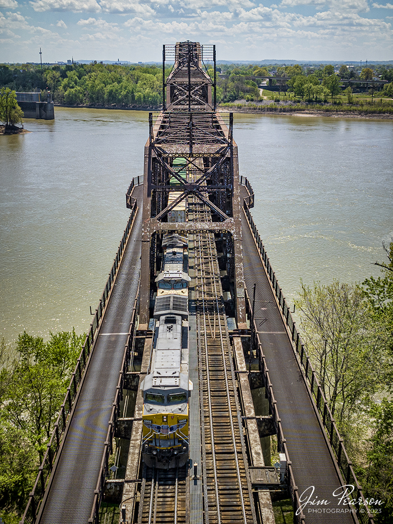 Union Pacific 6808 and 2659 lead Norfolk Southern 224 over the K&I bridge out of Louisville, Kentucky as they head west over the Ohio River into New Albany, Indiana on the NS Southern East District on April 15th, 2023.

According to Wikipedia: The Kentucky & Indiana Bridge is one of the first multi modal bridges to cross the Ohio River. It is for both railway and common roadway purposes together. By federal, state, and local law railway and streetcar, wagon-way, and pedestrian modes of travel were intended by the City of New Albany, City of Louisville, State of Kentucky, State of Indiana, the United States Congress, and the bridge owners. 

The K & I Bridge connects Louisville, Kentucky to New Albany, Indiana. Constructed from 1881 to 1885 by the Kentucky and Indiana Bridge Company, the original K&I Bridge opened in 1886. It included a single standard gauge track and two wagon ways, allowing wagons and other animal powered vehicles to cross the Ohio River by a method other than ferry for the first time. At the time motorized vehicles were virtually nonexistent. 

The K&I Bridge company also owned a ferry boat operation during both the 1st and 2nd bridge; eventually that operation was sold as the bridge's success largely outmoded boat usage.

In 1910 the bridge company was renamed the Kentucky & Indiana Terminal Railroad Co. From 1910 to 1912, a new, heavier bridge was built on new piers just upstream from the original one, after which the old bridge was demolished. The new bridge was double tracked to handle increasingly heavier train and now automobile traffic, eventually receiving the U.S. 31W designation.

The bridge also featured a rotating swing span opening for the passage of ships in high water. The bridge was only opened four times, twice for testing in 1913 and 1915, then in 1916 for the passage of the steamer "Tarascon" and in 1920 for passage of the Australian convict ship "Success". In 1948 it refused opening of the span for passage of the steamer "Gordon C. Greene" citing inconvenience and costs of cutting power and communication lines, an action for which K&I and LG&E both paid damages to that ship's company. In 1955 the K&I sought and received permission to permanently tie down the swing span from the Corps of Engineers. In 1952, the creosoted wood block roadways of the second bridge were eliminated and replaced by a steel gridwork roadway.

On February 1, 1979, an overweight dump truck caused a small segment of the steel grate roadway on the bridge to sag about 1 foot (0.30 m). A quick survey promised to reopen the roadway, but automotive traffic was banned thereafter by the railroad.

Tech Info: DJI Mavic 3 Classic Drone, RAW, 24mm, f/2.8, 1/2500 sec, ISO 130.

#trainphotography #railroadphotography #trains #railways #dronephotography #trainphotographer #railroadphotographer #jimpearsonphotography #kentuckytrains #mavic3classic #drones #trainsfromtheair #trainsfromadrone #KandIbridge #LouisvilleKy #NSsoutherneast #norfolksouthern