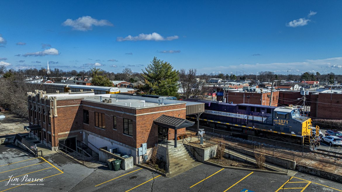 Atlantic Coast Line Heritage Unit CSXT 1871 passes the old L&N Depot in downtown Madisonville, Ky, on January 31st, 2025, as it leads hot intermodal I025 southbound on the CSX Henderson Subdivision.

According to a CSX Press Release: November 29, 2023 – The CSX fleet of heritage locomotives is continuing to grow with the introduction of a unit painted in a custom design honoring the Atlantic Coast Line Railroad.

Designated CSX 1871, the seventh locomotive in the heritage series was unveiled at the CSX Locomotive Shop in Waycross, Georgia, which has designed and applied the paint schemes for all the heritage units. The latest in the series features the modern CSX design on the head end, transitioning to historic paint scheme and logo of the Atlantic Coast Line at the rear.

The Atlantic Coast Line name first appeared in 1871, and the American Coast Line Railroad (ACL) was officially incorporated in 1900. The ACL extended from Georgia to Richmond, Virginia, and later expanded into Florida. In 1960, the company opened a new headquarters building in Jacksonville, which continues as CSX headquarters to this day. The ACL merged with the Seaboard Air Line Railroad in 1967 to form the Seaboard Coast Line, which later became part of CSX.

“We do a lot of research on the colors and the schemes just to make sure that we get it right,” said Jeromy Hutchison, CSX carman painter. “We want to make sure we do our heritage justice.”

CSX 1871 will carry the ACL colors in service across the 20,000-mile CSX network, reinforcing employee pride in the history of the railroad that continues to move the nation’s economy with safe, reliable and sustainable rail-based transportation services.

Tech Info: DJI Mavic 3 Classic Drone, RAW, 22mm, f/2.8, 1/2000, ISO 100.

#trainphotography #railroadphotography #trains #railways #jimpearsonphotography #onecsx #csxheritageunits