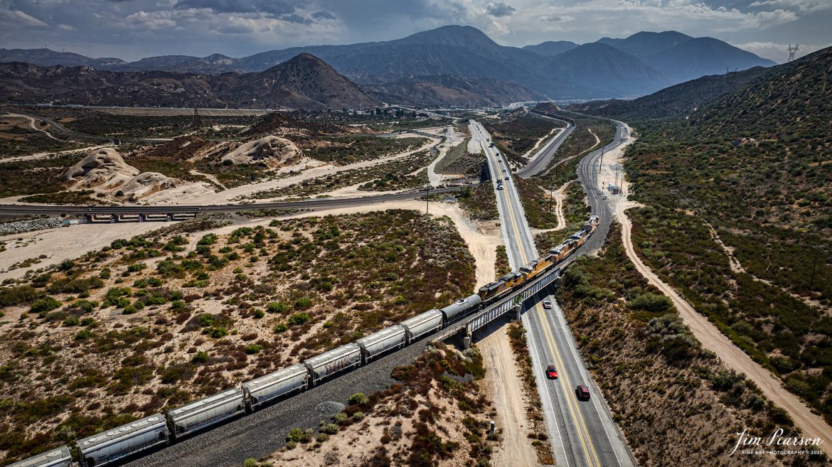 A westbound Union Pacific freight heads downhill through the Cajon Pass in southern California, as they cross over Hwy 138  on September 20th, 2024, on the BNSF Cajon Subdivision.   

According to Wikipedia: Cajon Pass is a mountain pass between the San Bernardino Mountains to the east and the San Gabriel Mountains to the west in Southern California. Created by the movements of the San Andreas Fault, it has an elevation of 3,777 ft (1,151 m). Located in the Mojave Desert, the pass is an important link from the Greater San Bernardino Area to the Victor Valley, and northeast to Las Vegas. The Cajon Pass area is on the Pacific Crest Trail.

Cajon Pass is at the head of Horsethief Canyon, traversed by California State Route 138 (SR 138) and railroad tracks owned by BNSF Railway and Union Pacific Railroad. Improvements in 1972 reduced the railroad's maximum elevation from about 3,829 to 3,777 feet while reducing curvature. Interstate 15 does not traverse Cajon Pass, but rather the nearby Cajon Summit. The entire area, Cajon Pass and Cajon Summit, is often referred to as Cajon Pass, but a distinction is made between Cajon Pass and Cajon Summit.

The California Southern Railroad, a subsidiary of the Atchison, Topeka and Santa Fe Railway, was the first railroad through Cajon Pass. The line through the pass was built in the early 1880s to connect the present-day cities of Barstow and San Diego. Today the Union Pacific Railroad and BNSF Railway (the successor to the Santa Fe) use the pass to reach Los Angeles and San Bernardino as part of the Southern Transcon. Due to the many trains, scenery and easy access, it is a popular location for railfans, and many photographs of trains on Cajon Pass appear in books and magazines.

The Union Pacific Railroad owns one track through the pass, on the previous Southern Pacific Railroad Palmdale cutoff, opened in 1967. The BNSF Railway owns two tracks and began to operate a third main track in the summer of 2008. The railroads share track rights through the pass ever since the Union Pacific gained track rights on the Santa Fe portion negotiated under the original Los Angeles and Salt Lake Railroad. 

Tech Info: DJI Mavic 3 Classic Drone, RAW, 24mm, f/2.8, 1/3200, ISO 130.

#railroad #railroads #train, #trains #railway #railway #steamtrains #railtransport #railroadengines #picturesoftrains #picturesofrailways #besttrainphotograph #bestphoto #photographyoftrains #bestsoldpicture #JimPearsonPhotography #trainsfromtheair #trainsfromadrone #CajonPass