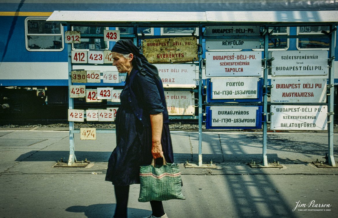 Film Wednesday – 1993 – Today’s slide scans are from time that I spent at the Budapest-Nyugati Railway Station, in Budapest, Hungry. I like this shot of the traveler all in black passing all the train destinations in the background.

According to Wikipedia, Budapest Nyugati station (Hungarian: Nyugati pályaudvar, pronounced [ˈɲuɡɒti ˈpaːjɒudvɒr]; lit. 'western railway station'), generally referred to simply as Nyugati, is one of the three main railway terminals in Budapest, Hungary. The station is on the Pest side of Budapest, accessible by the 4 and 6 tramline and the M3 metro line.

The station was designed by Auguste de Serres and was built by the Eiffel Company. It was opened on 28 October 1877. It replaced another station, which was the terminus of Hungary's first railway line, the Pest–Vác line (constructed in 1846). This building was demolished to construct the Grand Boulevard.

The station got its name from the adjacent Western Square ('Nyugati tér'), a major intersection where Teréz körút (Theresia Boulevard), Szent István körút (Saint Stephen Boulevard), Váci út (Váci Avenue), and Bajcsy-Zsilinszky út (Bajcsy-Zsilinszky Avenue) converge. The square also serves as a transport hub with several bus routes, tram routes 4 and 6, and a station on M3 of the Budapest Metro.

Beside the terminal and partially above its open area there is the WestEnd City Center shopping mall. Inside the station is a McDonald's restaurant which has been described as the "most elegant" McDonald's in the world.

The music video for Gwen Stefani's 2008 single Early Winter was partly shot at Nyugati. Starting in May 2016 the key scenes of the movie Terminal were shot over 27 nights.

Tech Info: Camera, Nikon F3, Ektachrome Slide Film, no other data recorded, Scanned with an PlusTek 82001i Film Scanner.

#slidescan #filmphotography #trains #railroads #jimpearsonphotography #FilmPhotography